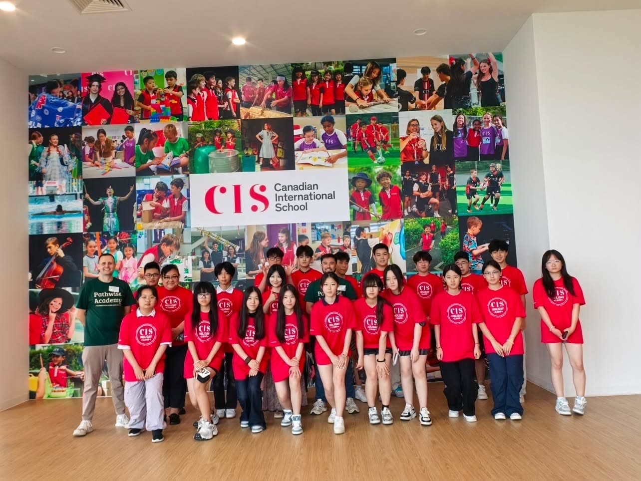 A large cohort of secondary students posed together in front of a school photo wall at the end of camp
