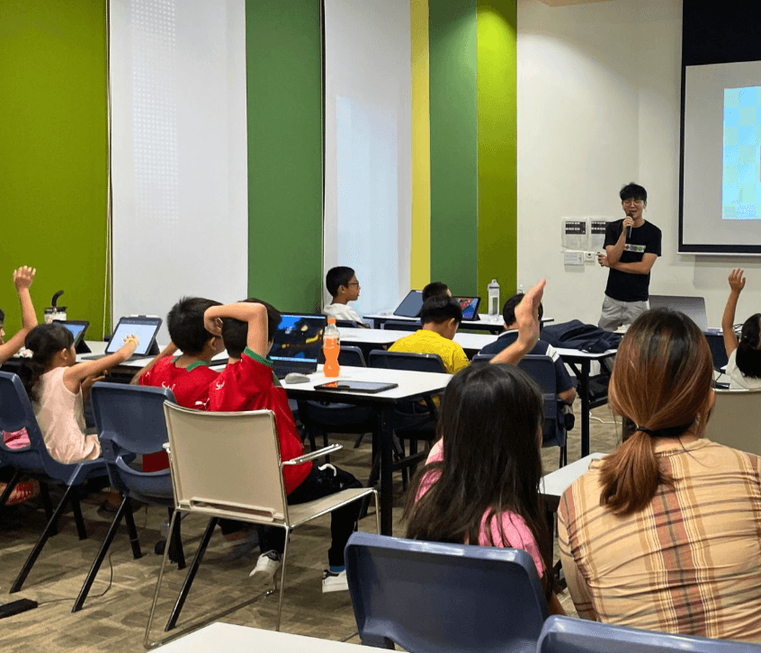 Younger learners in a Pathwise classroom raising hands while a Pathwise teacher teaches