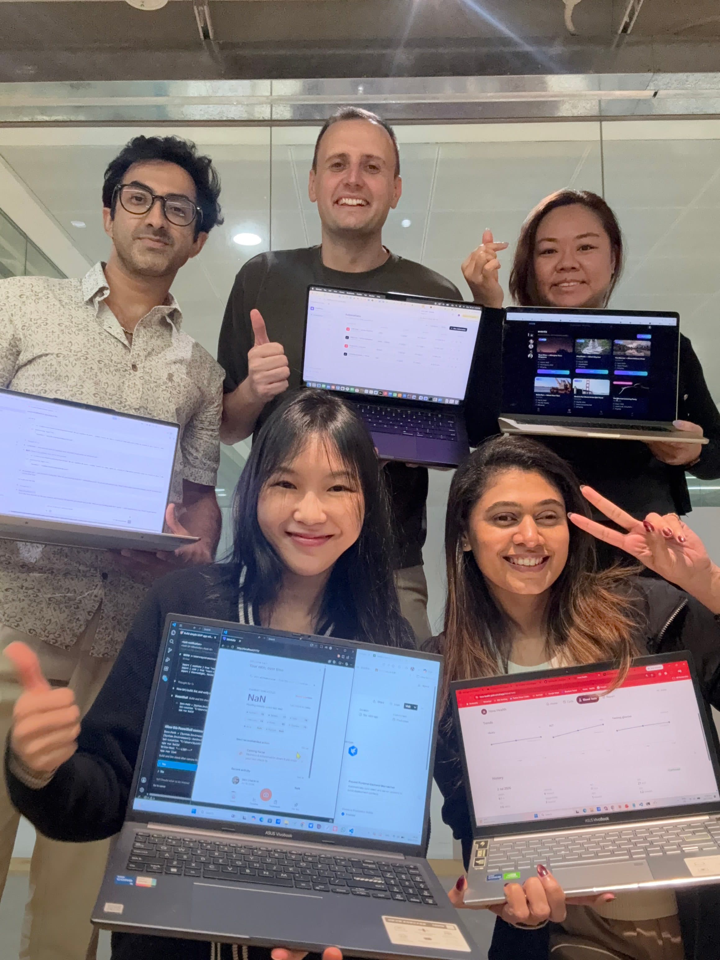 Adult cohort students holding up their laptops, each showing a different app they built in class